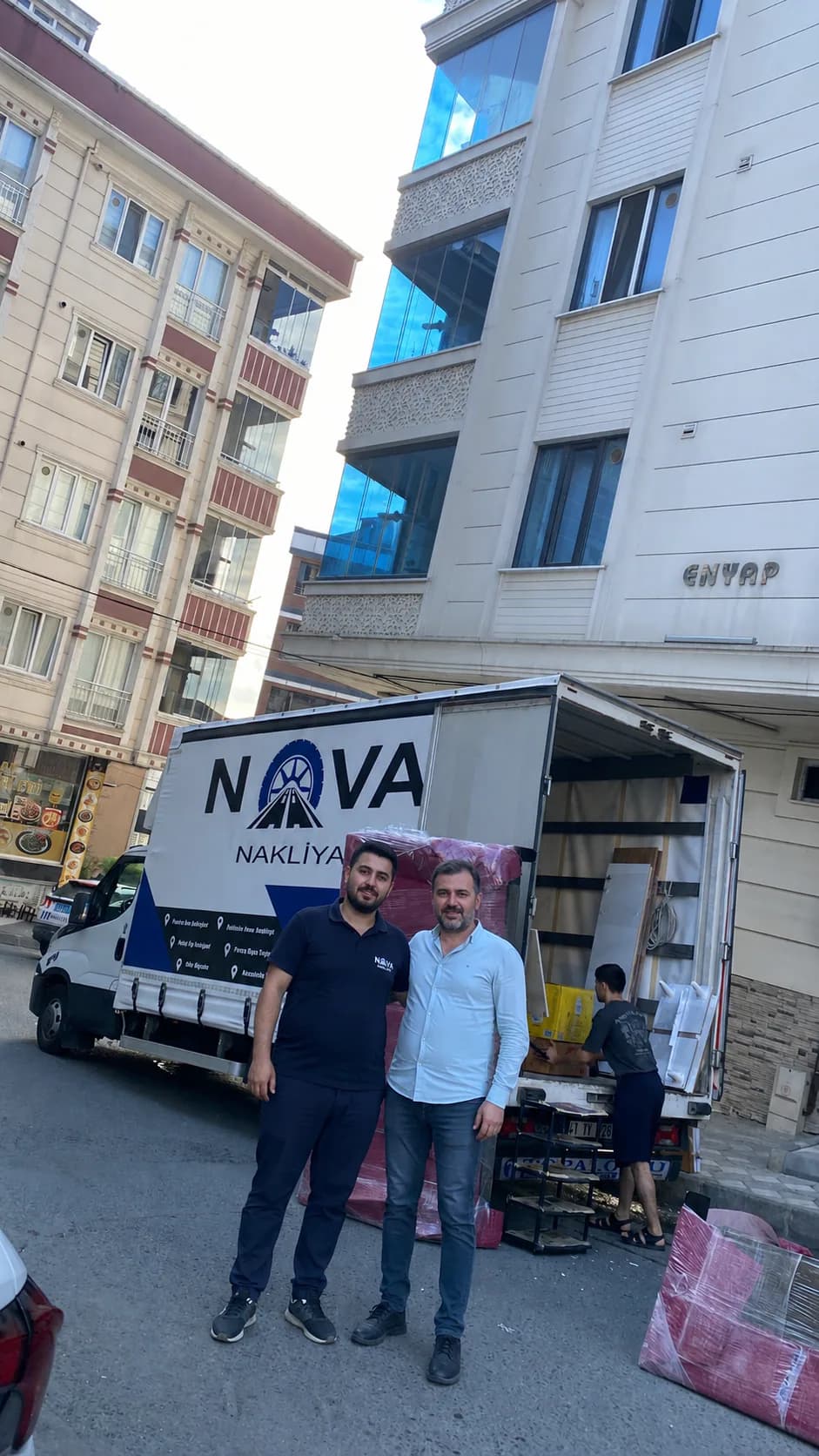 Nova Nakliyat çalışanı ve müşteri, ambalajlı eşyaların yüklendiği logolu nakliye kamyonunun önünde