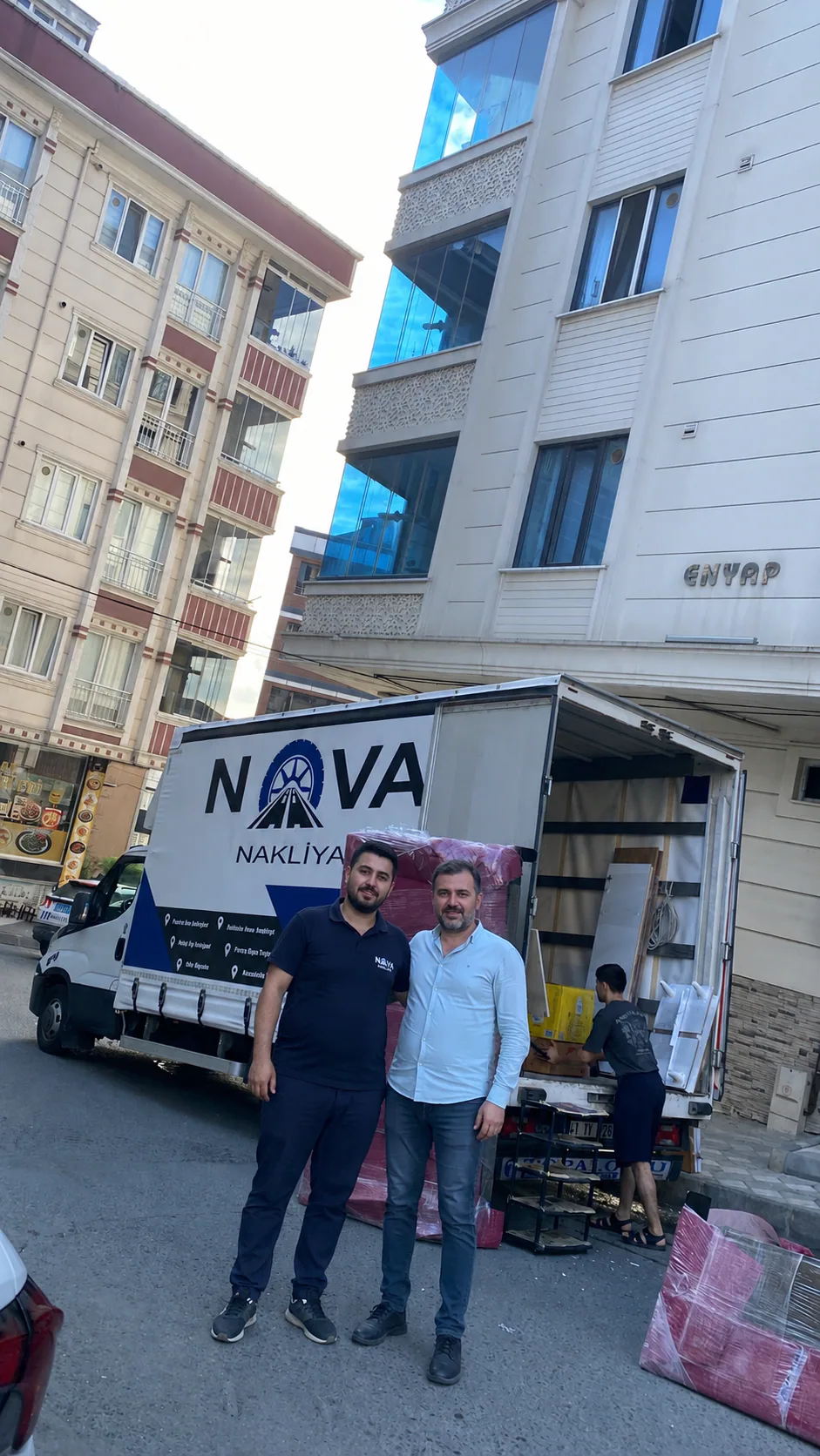Nova Nakliyat çalışanı ve müşteri, ambalajlı eşyaların yüklendiği logolu nakliye kamyonunun önünde
