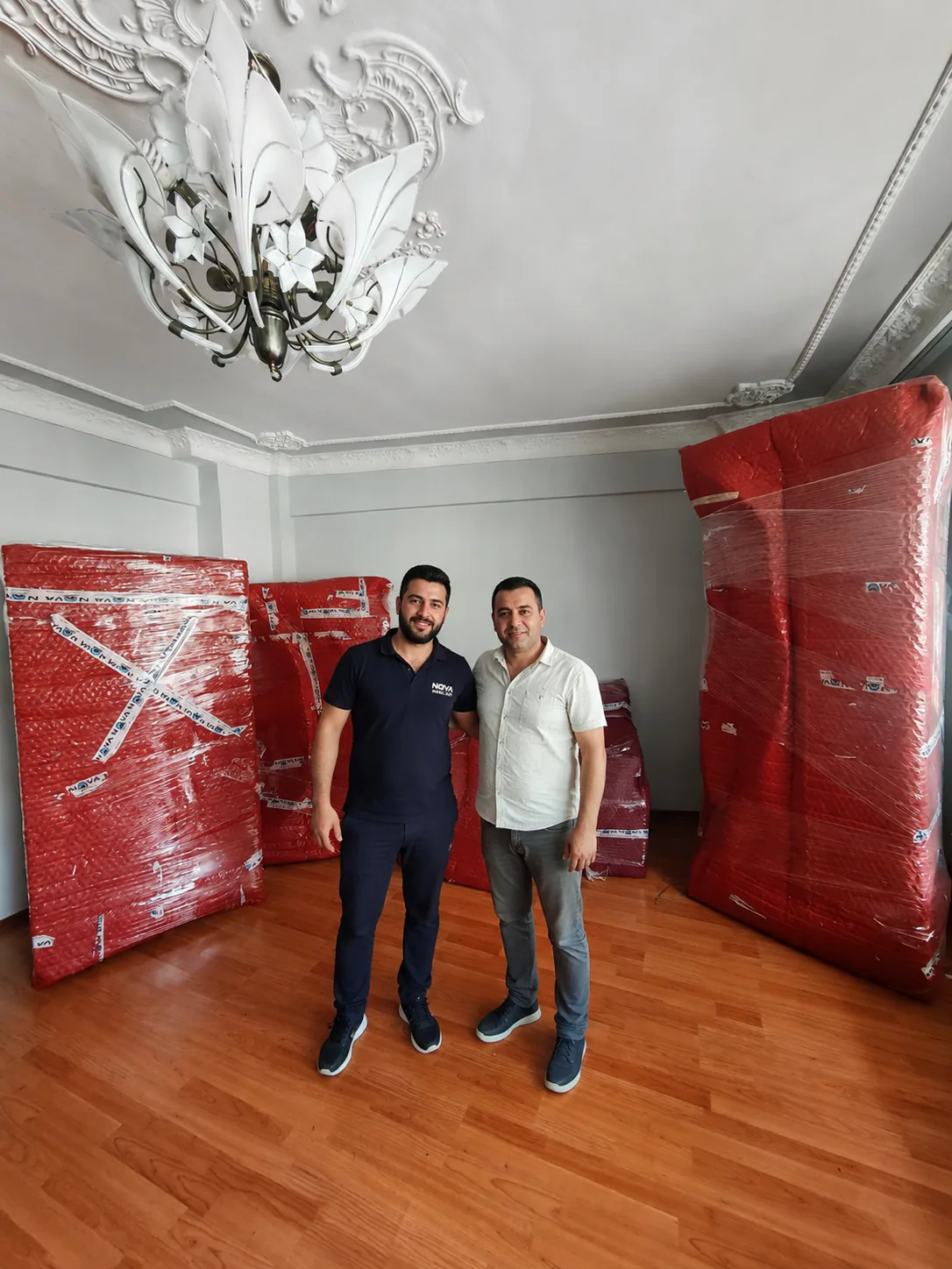 Nova Nakliyat çalışanı ve müşteri, kırmızı koruyucu ambalajla paketlenmiş ev eşyalarının önünde